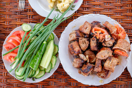On the wicker table plates with pieces of shashlik, porridge and vegetables. Summer dinner in the open air. Top view.の写真素材
