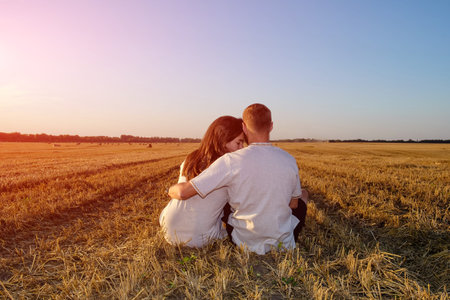 Girl and her boyfriend in a field of harvested wheat and hugging sitting back to the camera.の写真素材