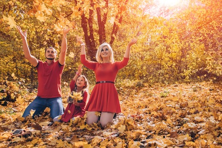 Beautiful young happy family throwing leaves in sunny warm autumn day. Concept of happy famiily relations, parenthood, carefree childhood. copy spaceの写真素材