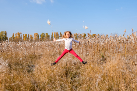 Little cute caucasian white girl jumping in a field with fluffy plants. Blue cloudless sky. Concept happy carefree childhood. copy spaceの写真素材