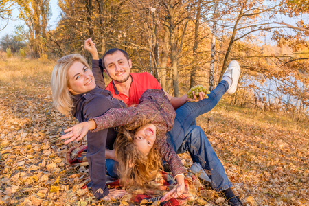 Bearded father hugs his wife and daughter. Young smiling family sitting on the autumn grass and having fun on a plaid. The concept of a happy family and carefree childhoodの写真素材