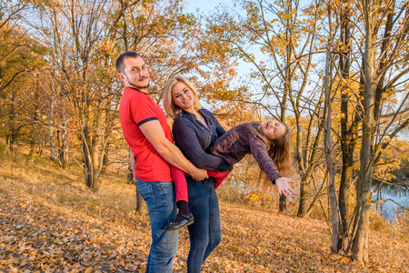 Bearded father hugs his wife and daughter. Young smiling family stands in the autumn park The concept of a happy family and parentingの写真素材