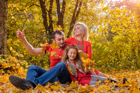 Beautiful young white family throwing leaves in sunny autumn day. Concept of happy one child family and parenting.の写真素材