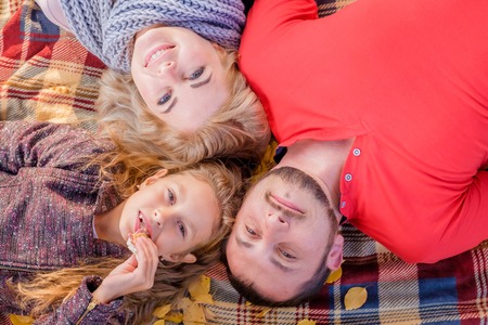 Young beautiful family lying on a plaid and smiling on a sunny autumn day. Little daughter eat sandwich. The concept of a happy family and family with one children.の写真素材