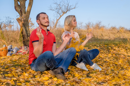 Young man and woman meditating in autumn park. Couple sitting outdoors on fall leaves. Concept body and mind.の写真素材