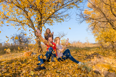 Beautiful young white family throwing leaves in sunny cloudless autumn day. Concept of happy family relations, parenting, joyful childhood.の写真素材