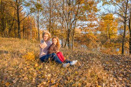 Beautiful mother and little cute daughter taking self portrait photo in the autumn park. Concept of one child family and single parentingの写真素材