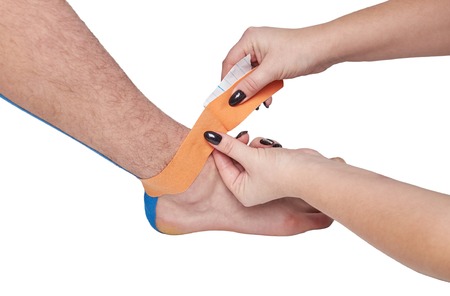 doctor physiotherapist hands applying kinesio medical taping on the ankle of a caucasian manの写真素材