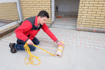 Electrician installing heating electrical cable on concrete floor. Man remove adgesive tape.の写真素材