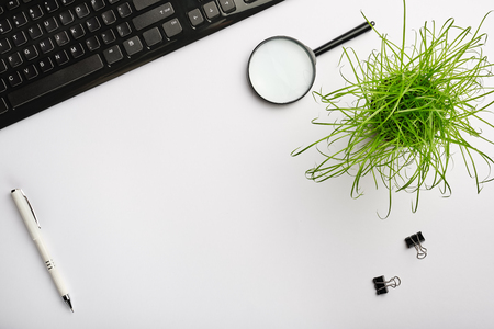 White surface of the table with keyboard, magnifying glass, clips, office plant and pen. Minimalistic work place.  Flat lay, copy space for your designの写真素材