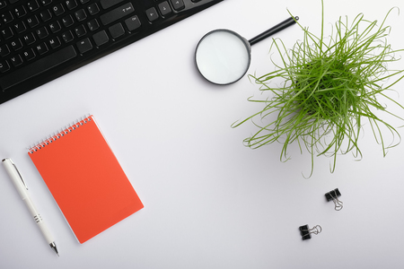 White surface of the table with keyboard, magnifying glass, notebook, clips, office plant and pen. Minimalistic work place.  Flat lay, copy space for your designの写真素材