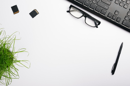 White surface of the table with keyboard, glasses, memory card and pen. Minimalist home office work place.  Flat lay, copy space for your designの写真素材