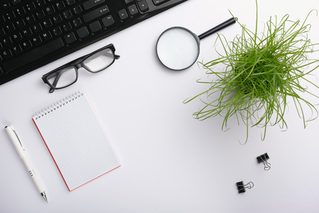 White surface of the table with keyboard, glasses, magnifying glass, notebook, clips, office plant and pen. Minimalistic work place.  Flat lay, copy space for your designの写真素材
