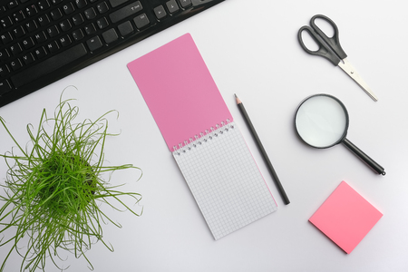 White surface of the table with keyboard, magnifying glass, notebook, scissors, office plant and pencil. home office work place concept. Flat lay, copy space for your designの写真素材