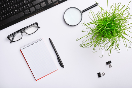 White table with keyboard, glasses, magnifying glass, notebook, clips, office plant and black pen. Minimalistic work place.  Flat lay, copy space for your designの写真素材