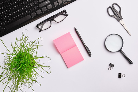 White table with keyboard, magnifying glass, stickers, scissors, office plant, clips and pen. home office work place concept. Flat lay, copy spaceの写真素材