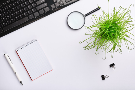White surface of the table with keyboard, magnifying glass, notebook, clips, office plant and pen. Minimalistic work place.  Flat lay, copy space for your designの写真素材