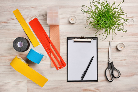 mock up with clipboard, rolls of colored kinesio tape, plant, scissors and other medical tools. alternative medicine workplace conceptの写真素材