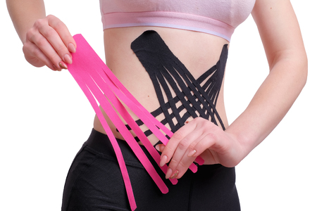 Hands of young girl applying pink kinesio tape on the her abdomen. isolated on wite backgroundの写真素材