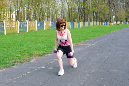 young white girl with kinesio tape on her belly and chest goes in for sports with dumbbells on old stadium track. Alternative medicine rehabilitationの写真素材