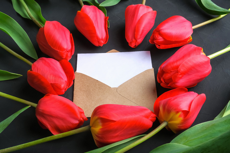 Mockup of fresh red tulips bouquet and greeting card in kraft envelope on dark background with copy space. Close up viewの写真素材