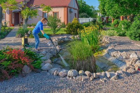 middle-aged white woman cleans a garden pond with high-pressure wash from sludge.の写真素材