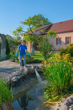 middle-aged white woman cleans a garden pond with high-pressure car wash near her own house.の写真素材