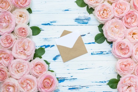 Flowers composition. Open envelope in the frame made of pink roses on aged white wooden background.の写真素材