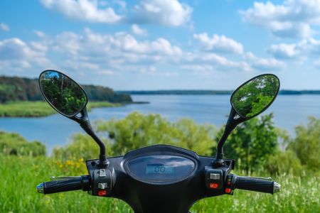 steering wheel of black electric scooter with reflection of trees in the mirrors on background of the river. Summer sunny dayの写真素材