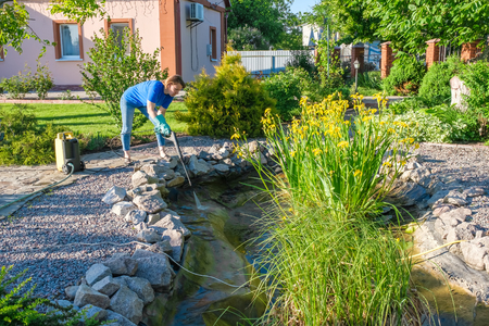 middle aged white woman cleans fish pond with high-pressure wash from sludge. Spring and summer pond care workの写真素材