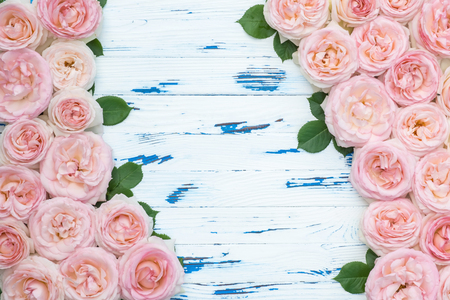 Flowers composition. Frame made of pink roses with leaves on aged white wooden background. Flat lay, top view, copy space.の写真素材