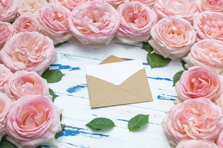 Flowers composition. Open craft paper envelope and leaves in the frame made of pink roses on aged wooden table. Flat lay, top view, copy space.の写真素材