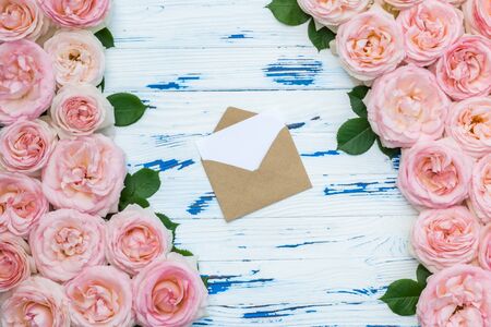 Flowers composition with open craft paper envelope in the frame made of pink roses on aged wooden background. Flat lay, top view, copy space.の写真素材