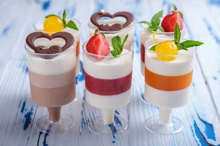 Six layered mousse desserts in wineglasses, decorated chocolate, strawberry, mint and cocktail cherries on aged wooden table. Closeup viewの写真素材