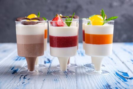 Layered mousse desserts in wineglasses, decorated chocolate, strawberry, mint and cocktail cherries on aged wooden table. Closeup viewの写真素材
