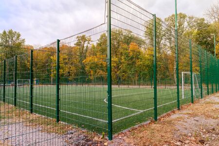 Mini-football court with artificial grass fenced with a green fence on a cloudy autumn dayの写真素材