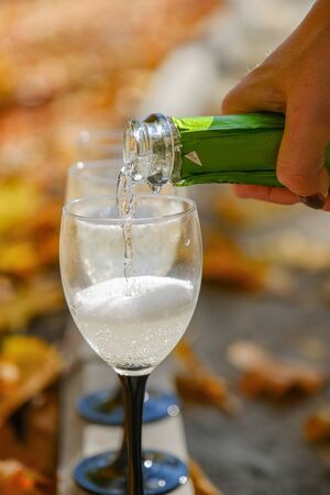Autumn Party and holiday celebration concept. The process of bottling champagne into three wineglasses on the garden path edge. view from the sideの写真素材
