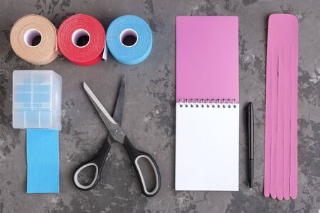 rolls kinesiology tape for athletes, scissors and notebook with pen on white background, top view. taping manipulate nerve receptors and reduces pain in muscles and speeds up the healing processの写真素材