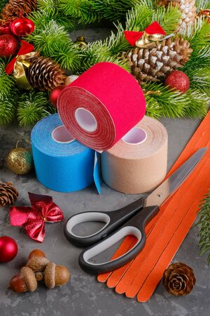 Christmas composition of wreath, fir, pine cones, balls, ribbons and stack of three rolls kinesiology tape for athletes and scissors on grey concrete background, vertical orientationの写真素材