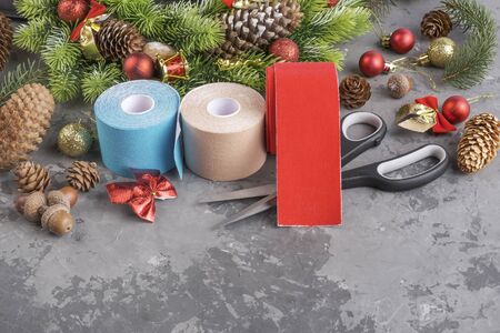 Christmas composition of wreath, fir, pine cones, balls, ribbons and stack rolls kinesiology tape for athletes and scissors on grey concrete background with copy spaceの写真素材