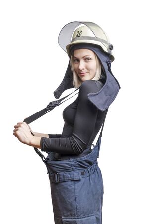 Young beauty firewoman pulls suspenders on her pants, smiling and looking to the camera isolated on white backgroundの写真素材