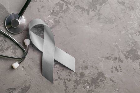 stethoscope and grey ribbon on concrete background. Parkinson's disease or brain cancer awareness symbolic concept to help support the campaign against illnessの写真素材
