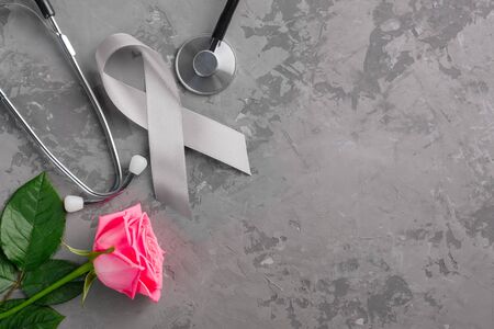 Grey ribbon, stethoscope and pink rose on a concrete background. Parkinsons disease or brain cancer awareness symbolic concept to help support the campaign against illnessの写真素材
