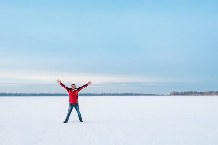 A happy smiling man with wide outstretched arms in the direction of clear sky, stands on the snowy surface of the frozen lakeの写真素材