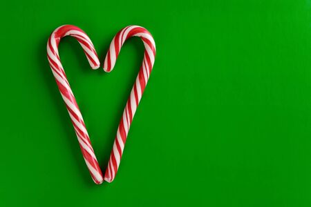 Two christmas red and white candy canes in the shape of heart on a green paper background. Copy space for text.の写真素材