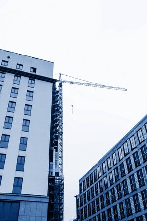 Top of building under construction with building crane, colored in trendy color of year 2020 Classic Blue. Foggy cloudy sky, copy spaceの写真素材