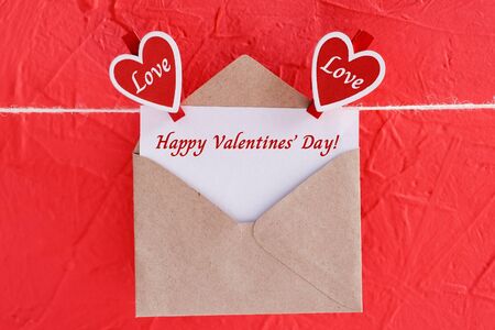 Inscription valentines day on card with craft envelope on red background and hearts on clothespins. Close up viewの写真素材