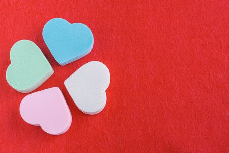 Assorted pink, blue, green and white pastel cosmetic sponges in heart shape on red felt background. skin care and beauty concept. Top viewの写真素材