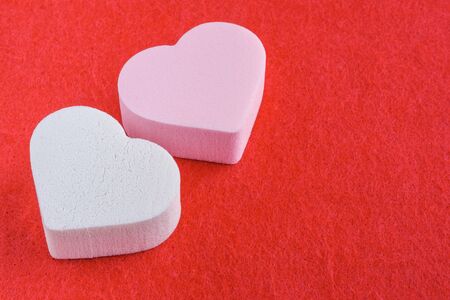 pink and white pastel cosmetic sponges in heart shape on red felt background. skin care and beauty concept. closeup viewの写真素材