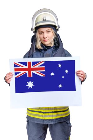 young beauty firefighter wearing uniform and helmet looking to the camera and holding paper sheet with australian flag in hands. isolated on white background.の写真素材